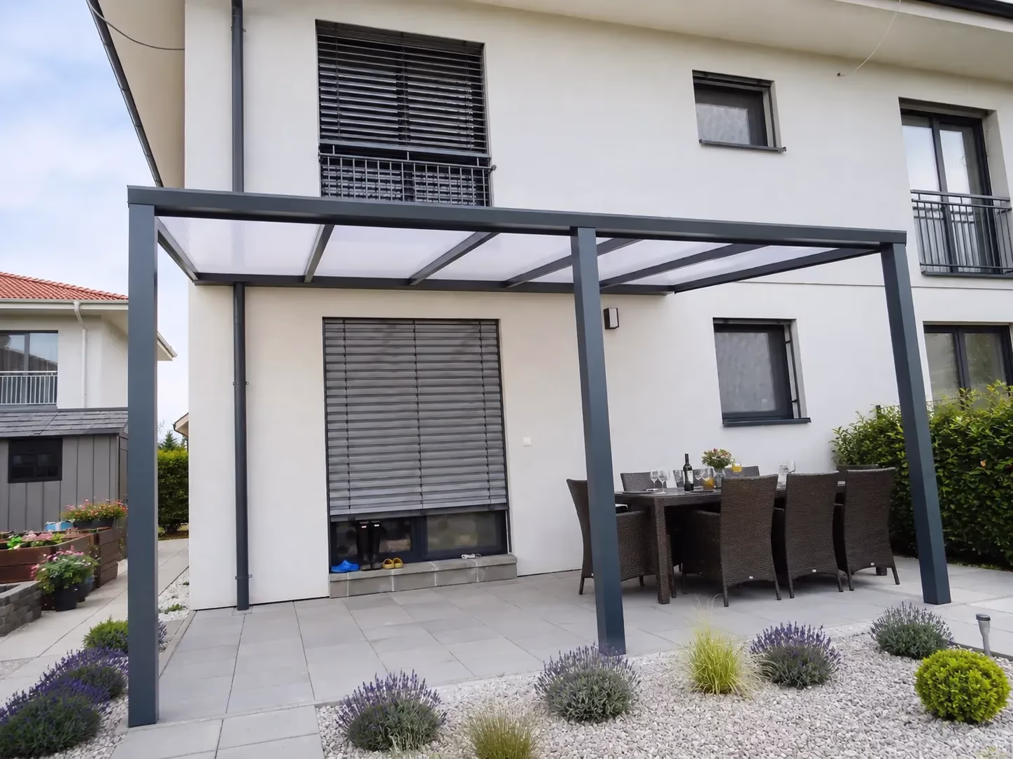 Anthrazitfarbene Aluminiumpergola Basic Class über einer Terrasse mit Esstisch neben einem Einfamilienhaus mit Lavendelgarten