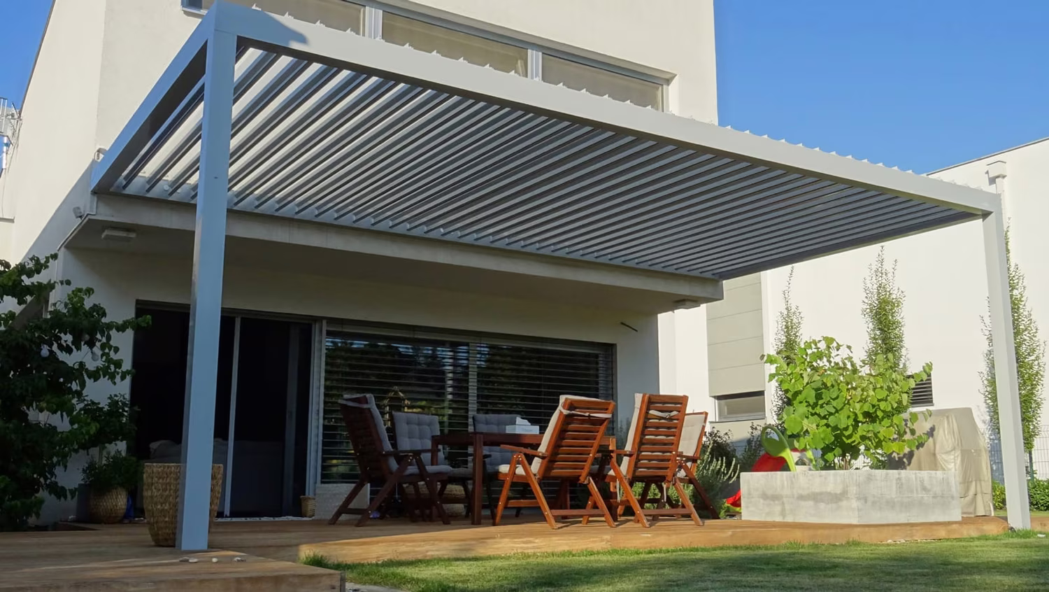 Bioklimatische Aluminiumpergola mit verstellbaren Lamellen über einer Terrasse mit Essgruppe an einem modernen Haus