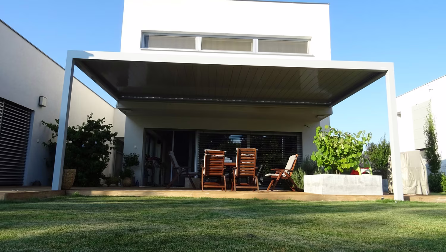 Bioklimatische Aluminiumpergola über einer Terrasse mit Sitzgelegenheit an einem modernen weißen Haus