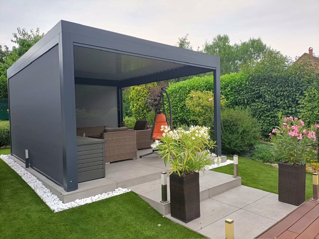 Anthrazitfarbene bioklimatische Aluminiumpergola mit seitlichem Screen und Rattanmöbeln im Garten