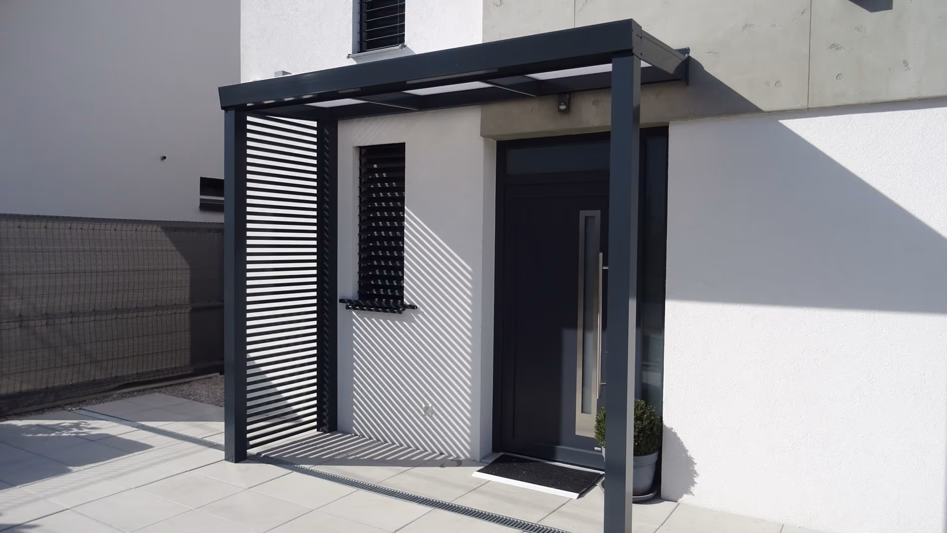 Aluminiumpergola Economic Class mit Loungesitzgruppe und Blumentöpfen