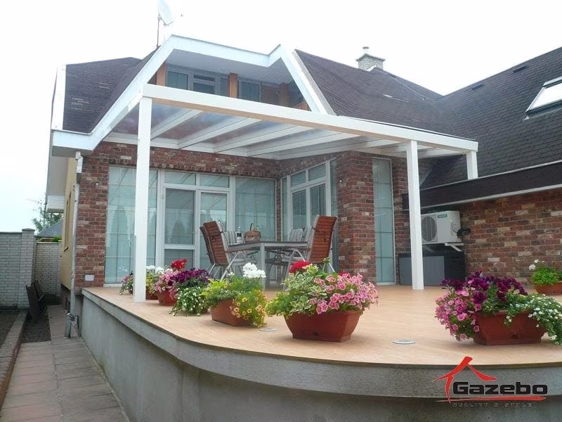 Weiße Aluminiumpergola Economic Class auf einer erhöhten Terrasse eines Ziegelhauses mit Blumenkästen
