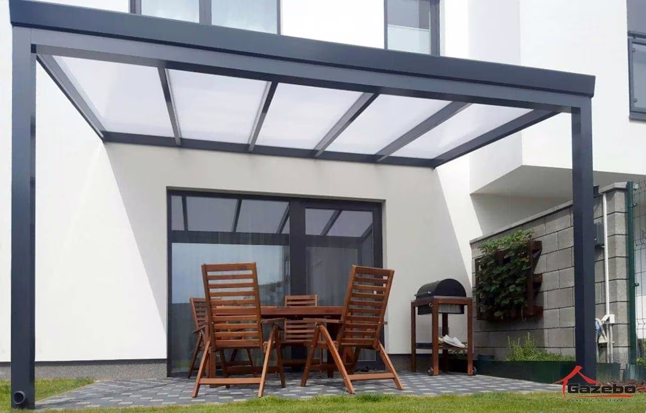 Anthrazitfarbene Aluminiumpergola Economic Class an einem weißen Haus mit Holztisch und Stühlen