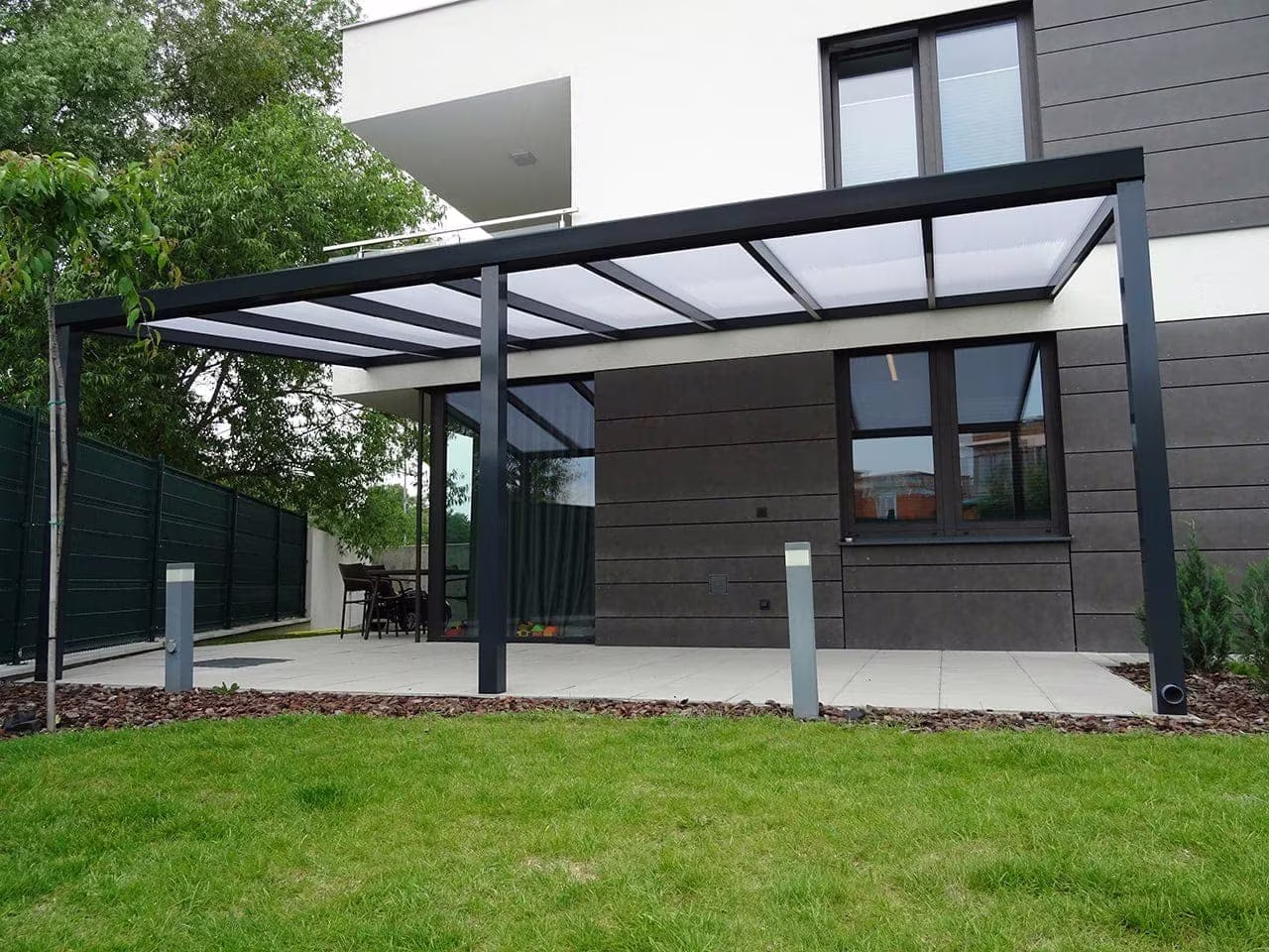 Anthrazitfarbene Aluminiumpergola Economic Class an einem modernen Haus mit Rasen