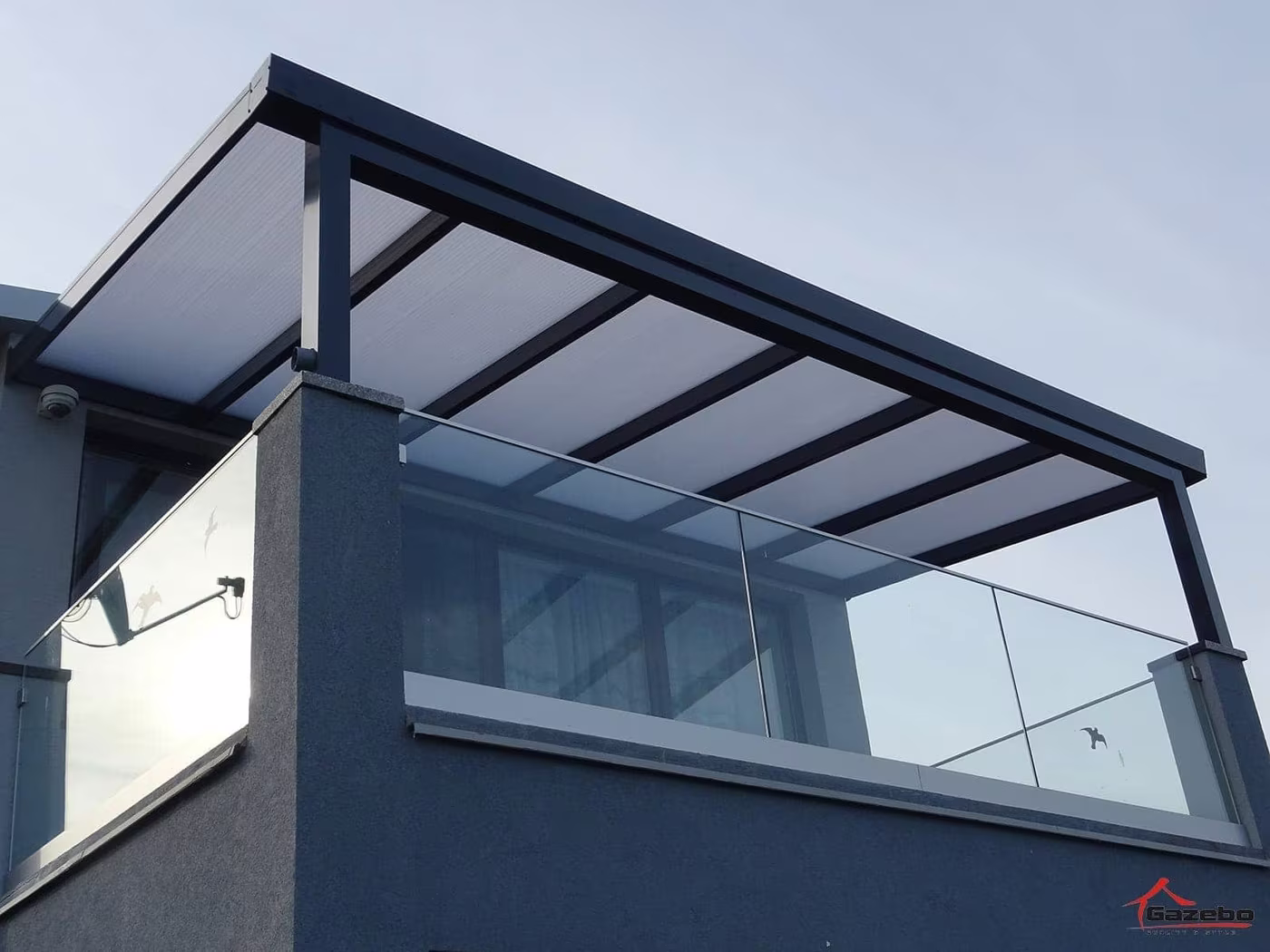 Nahaufnahme einer anthrazitfarbenen Aluminiumpergola Economic Class mit Glasgeländer und Polycarbonatdach