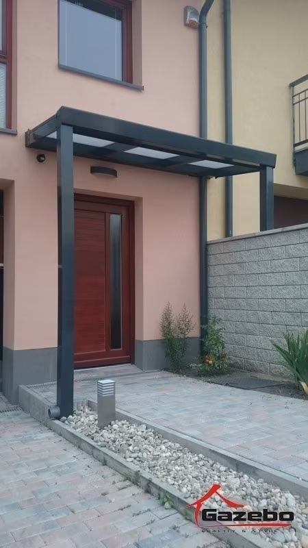Anthrazitfarbene Aluminiumpergola Economic Class als Vordach über dem Eingang eines rosa Hauses