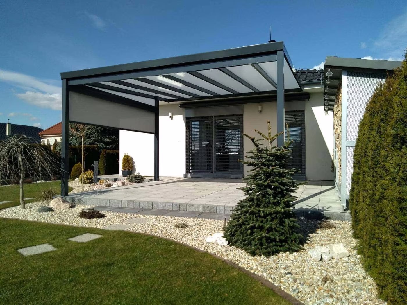Anthrazitfarbene Aluminiumpergola Economic Class an einem modernen weißen Haus mit gepflegtem Garten