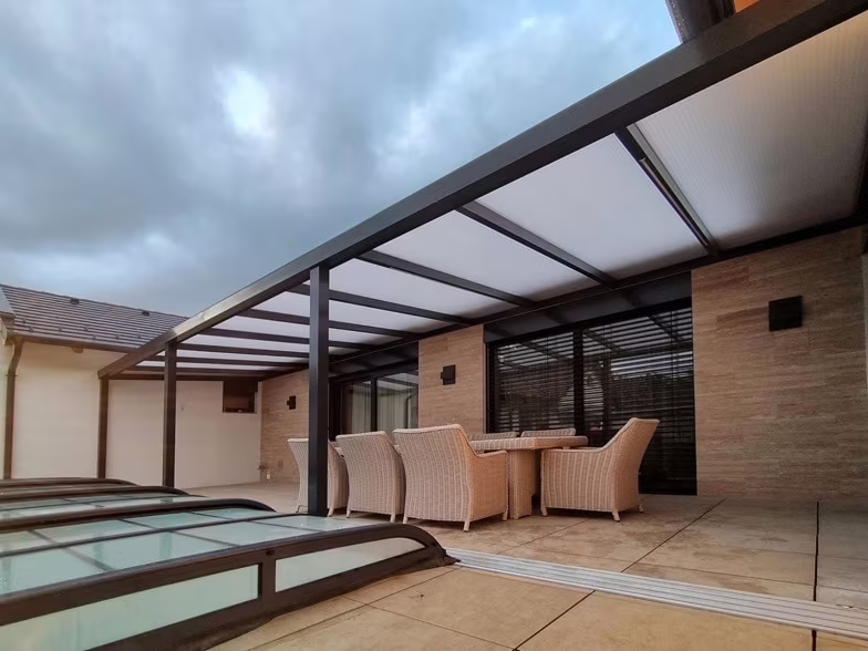 Anthrazitfarbene Aluminiumpergola Economic Class über einem überdachten Pool mit Rattanmöbeln
