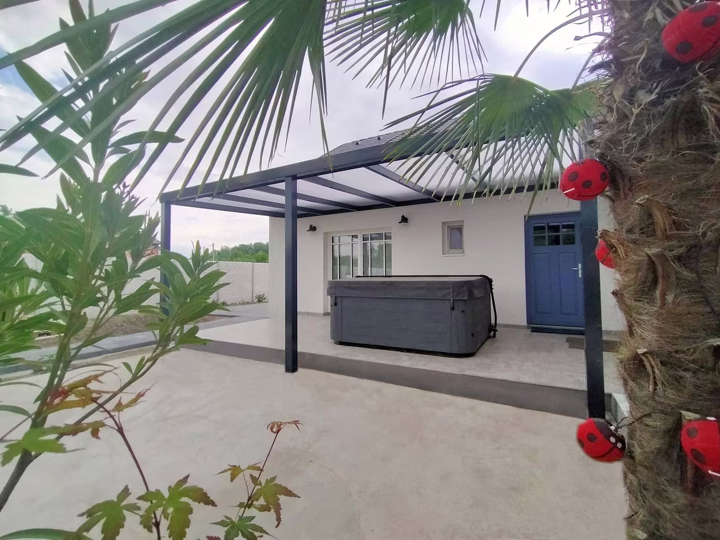 Anthrazitfarbene Aluminiumpergola Economic Class mit Whirlpool und Palme neben einem Haus