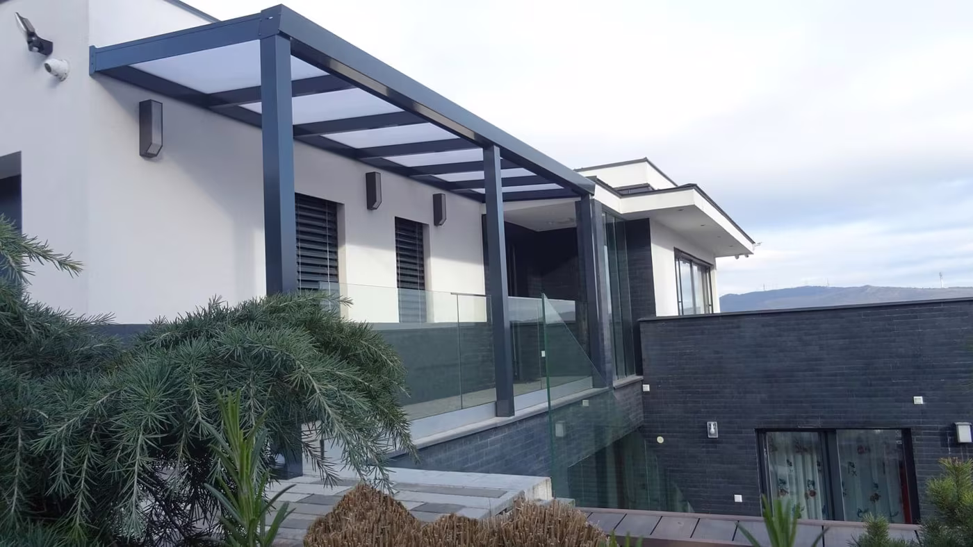 Anthrazitfarbene Aluminiumpergola Economic Class an einem modernen grauen Haus mit Glasgeländer