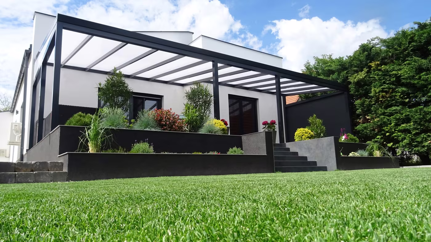 Anthrazitfarbene Aluminiumpergola Economic Class über einer Terrasse auf einem Hanggrundstück mit Rasen
