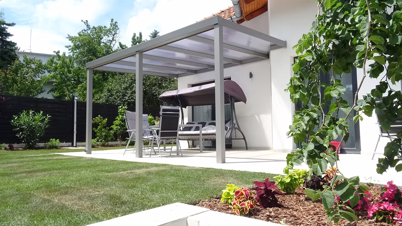Anthrazitfarbene Aluminiumpergola Economic Class über einer gepflasterten Fläche zwischen Häusern mit Sitzecke