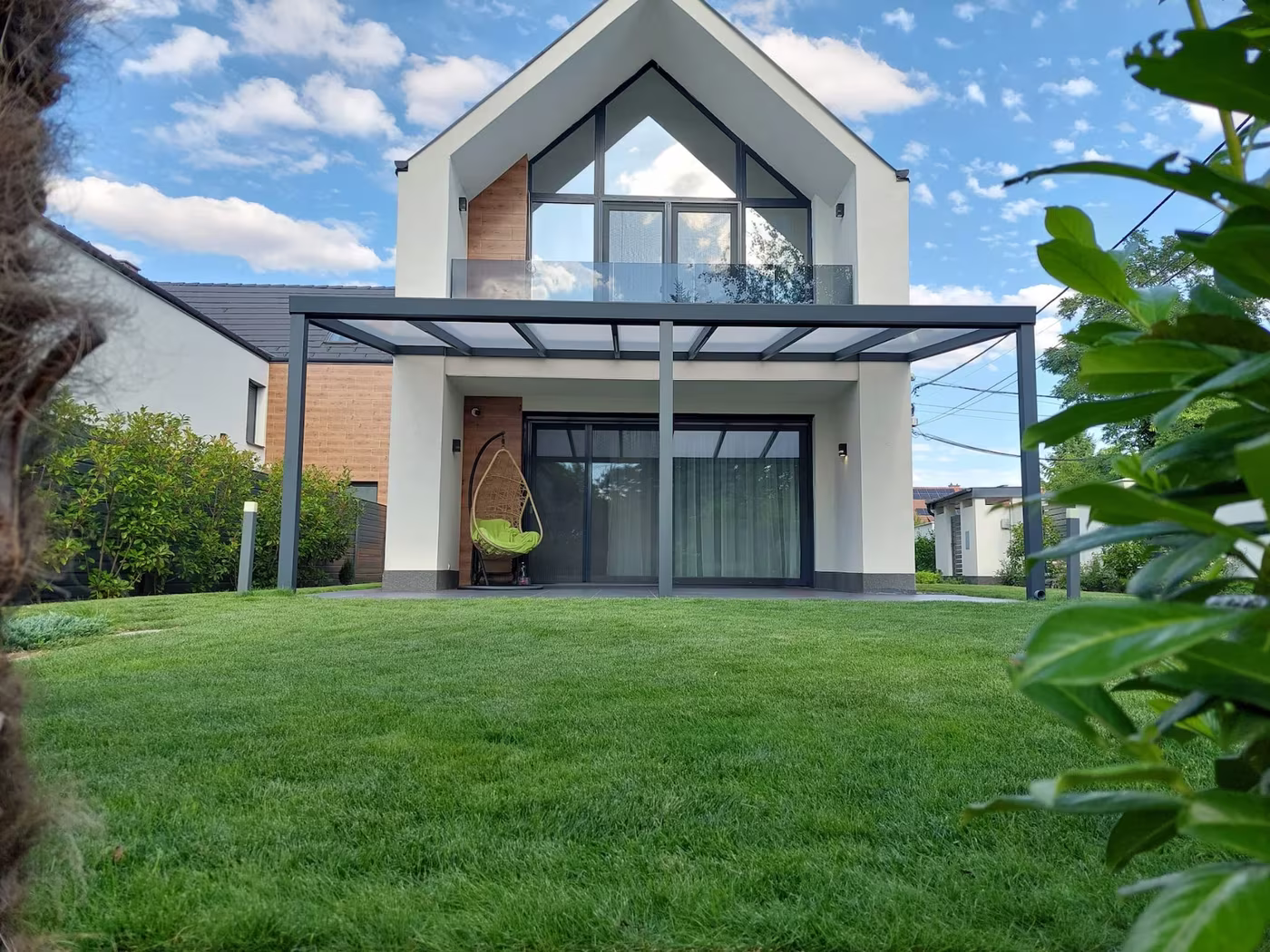 Anthrazitfarbene Aluminiumpergola Economic Class über der Terrasse eines modernen Hauses mit Satteldach