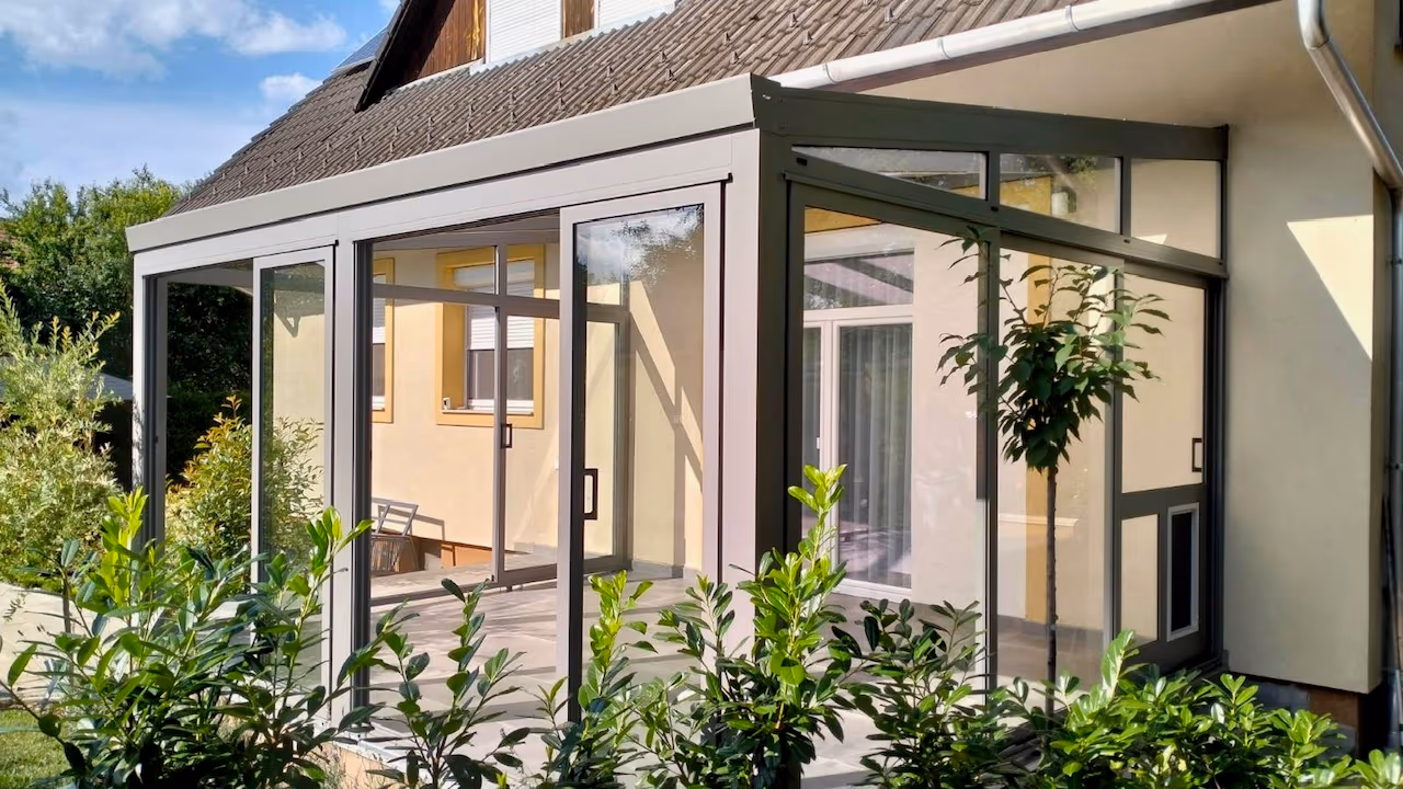 Wintergarten Economic Garden mit Glas-Schiebetüren neben einem gelben Einfamilienhaus