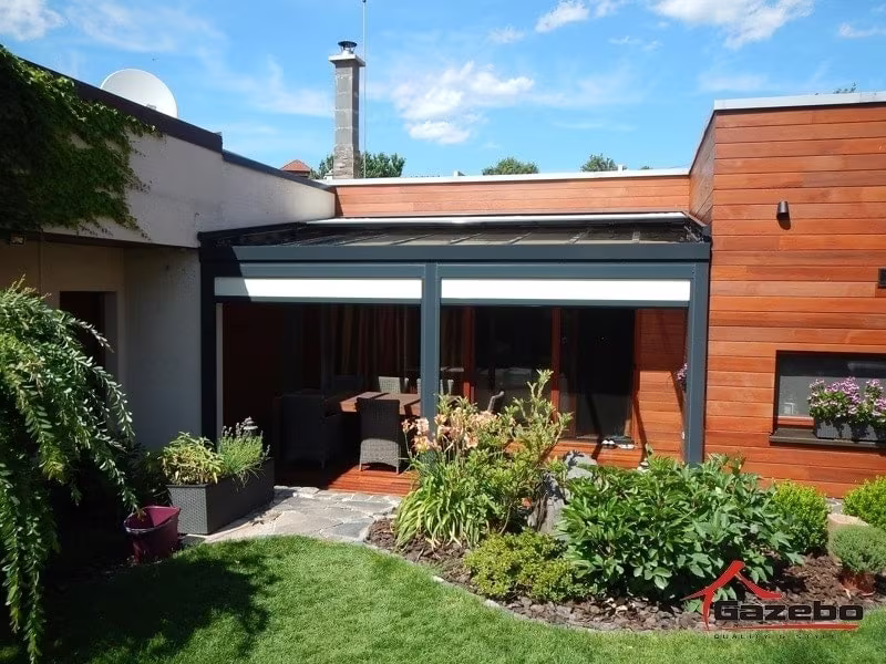 Anthrazitfarbene Aluminiumpergola Top Class über einer Terrasse mit Sitzgelegenheit an einem holzverkleideten Haus