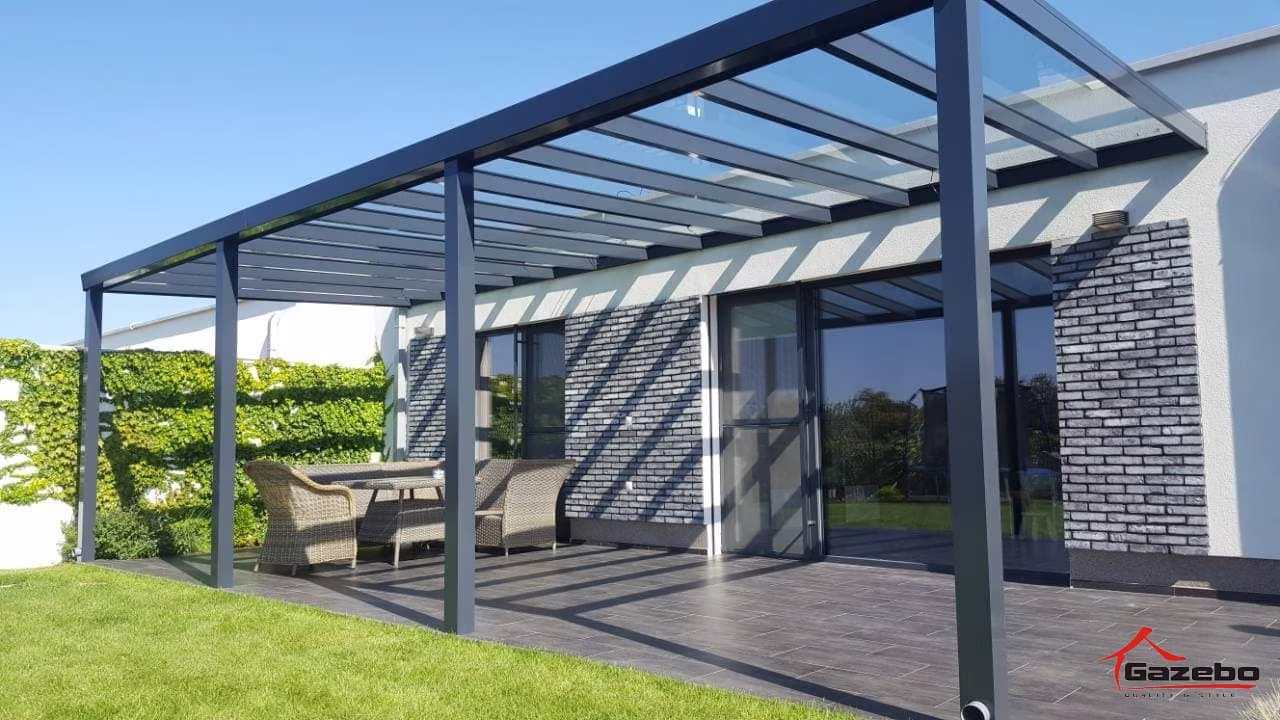 Anthrazitfarbene Aluminiumpergola Top Class über einer Holzterrasse mit Rattanmöbeln an einem modernen Haus