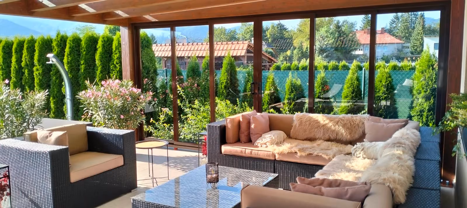 Eingerichtete Holzpergola Milano mit großer Sitzgruppe bei einem Haus mit rotem Dach
