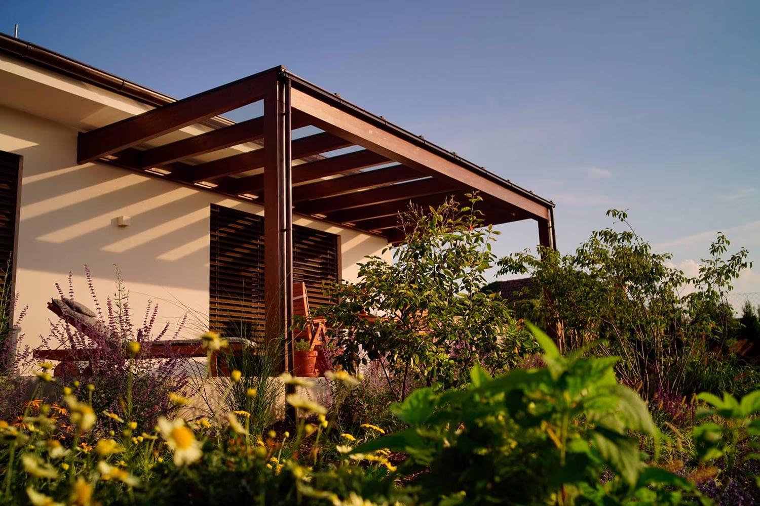 Holzpergola Milano mit einer Lamellen-Holzseite und einem Blumengarten