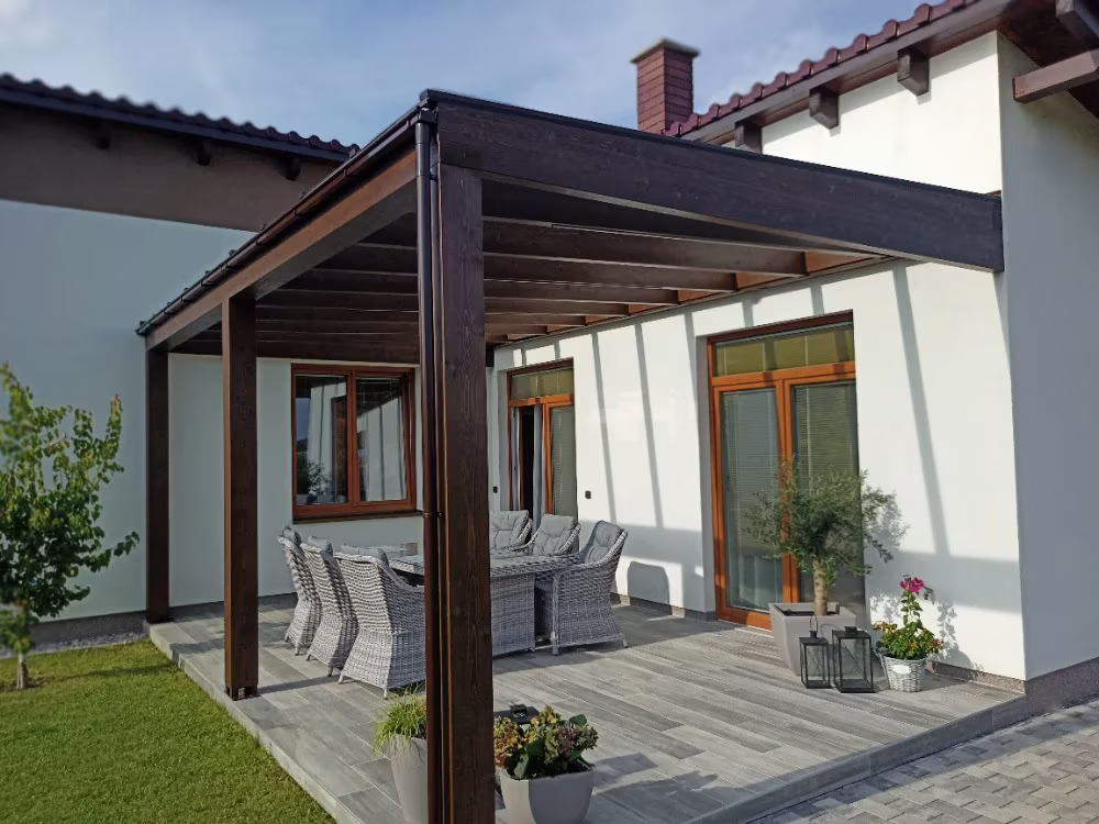 Holzpergola Milano über einer Terrasse mit Sitzgelegenheit an einem Einfamilienhaus