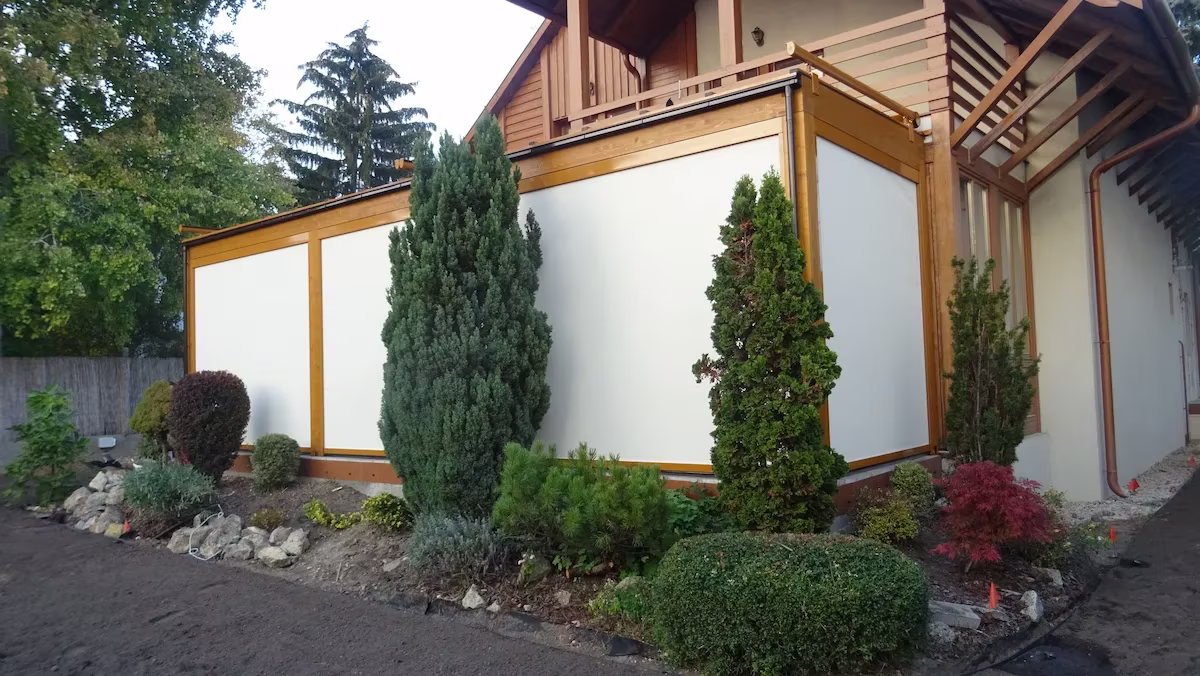 Holzpergola Milano mit Verglasung und einem gepflegten Garten