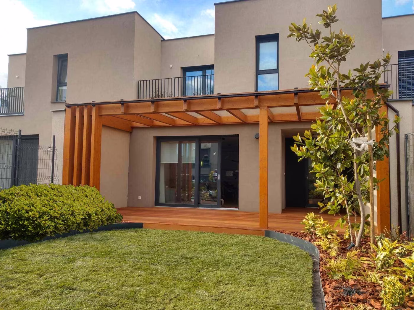 Holzpergola Fenix an einem modernen zweigeschossigen Haus über einer Holzterrasse